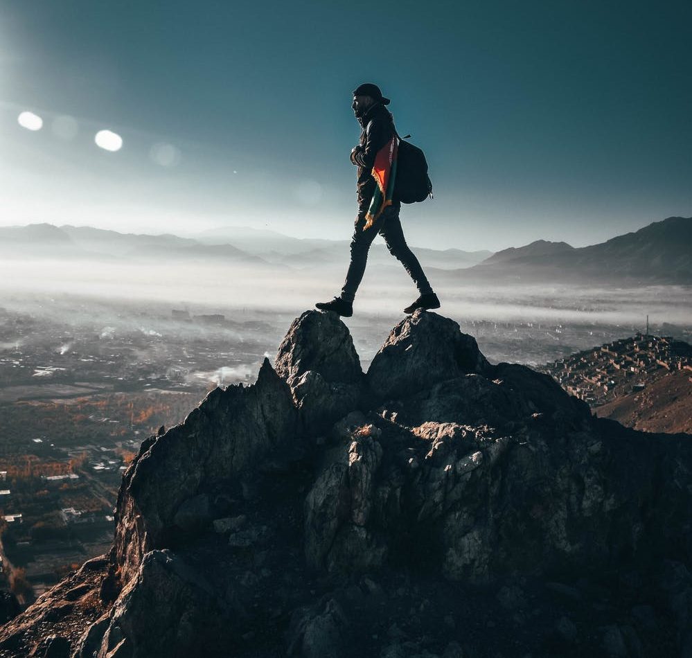Foto di un ragazzo sulla punta di una montagna con un cielo sereni e soleggiato