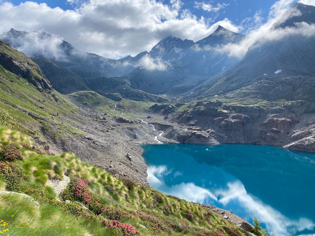 Vista lago nitido in mezzo alle montagne verdi e coperte con chiazze di neve su un cielo nuvoloso