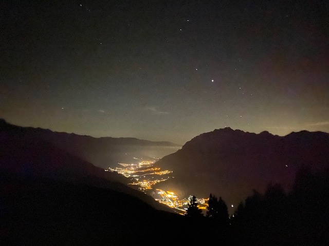 Foto notturna di un cielo stellato e una distesa di montagne illuminate da una serie di luci artificiali