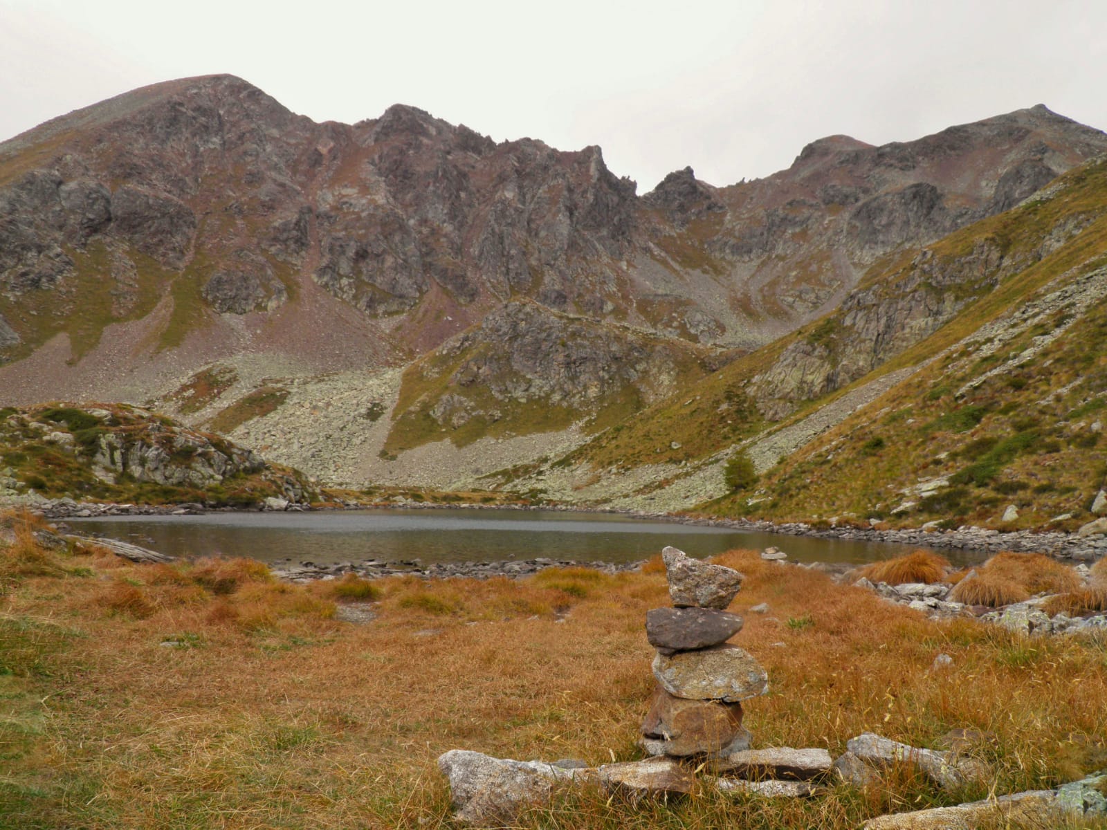 Foto di un piccolo lago circondato da piccole rocce e montagne con erba appassita