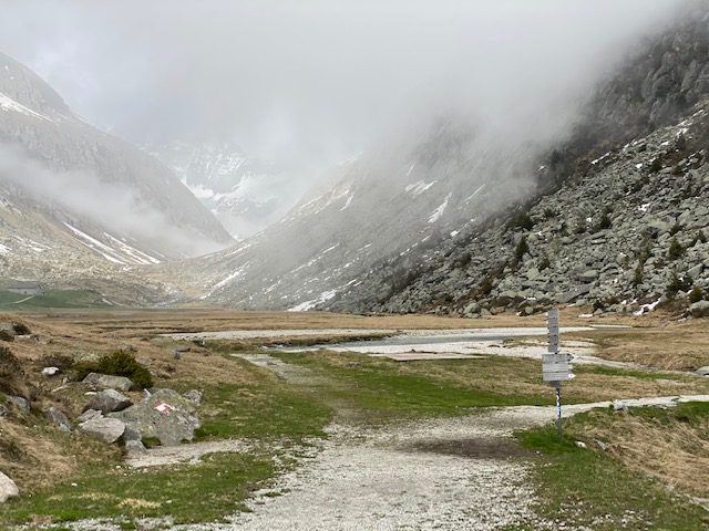 Vista in primo piano di un pannello con indicazioni e in secondo piano delle montagne rocciose coperte di di nebbia