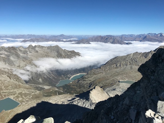 Vista dall'alto di un lago circondato da alte montagne che toccano e superano le nuvole su un cielo cristallino