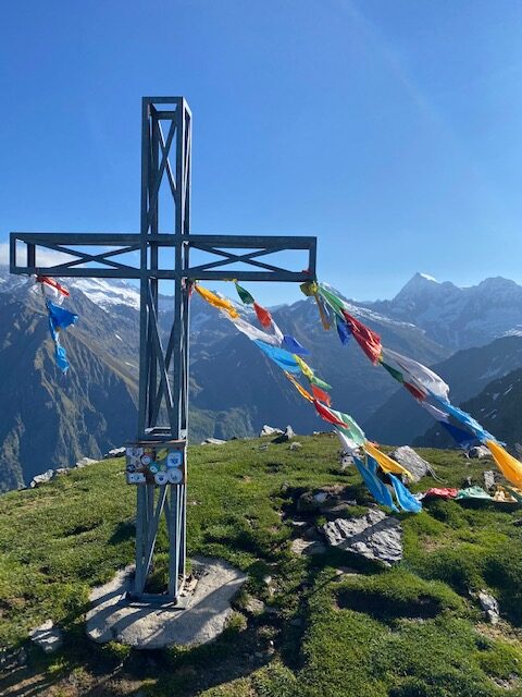 Foto di una croce in acciaio in cima alla montagna con delle piccole bandierine colorate