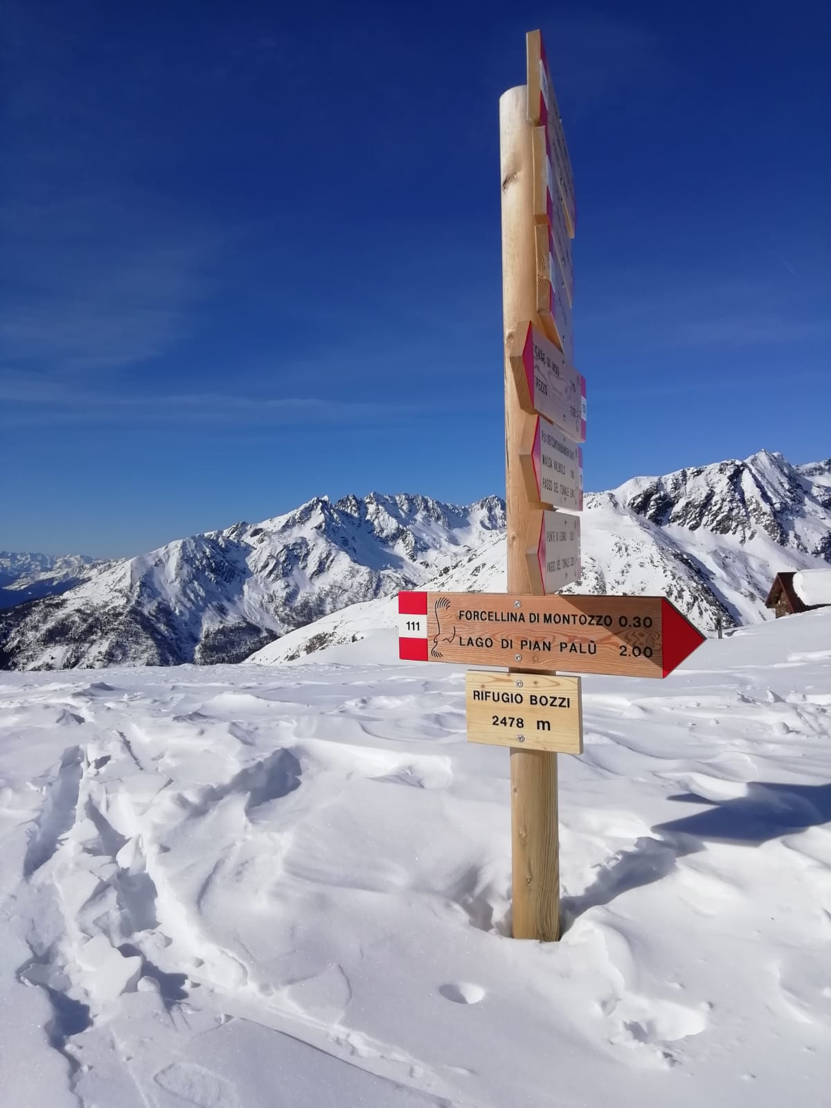 Foto di un palo con varie indicazioni installato in mezzo alla neve in montagna