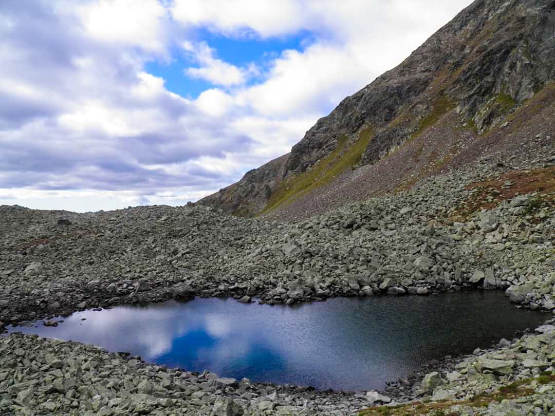 Vista di uno piccolo stagno circondato da piccole rocce che rispecchia la limpidità del cielo