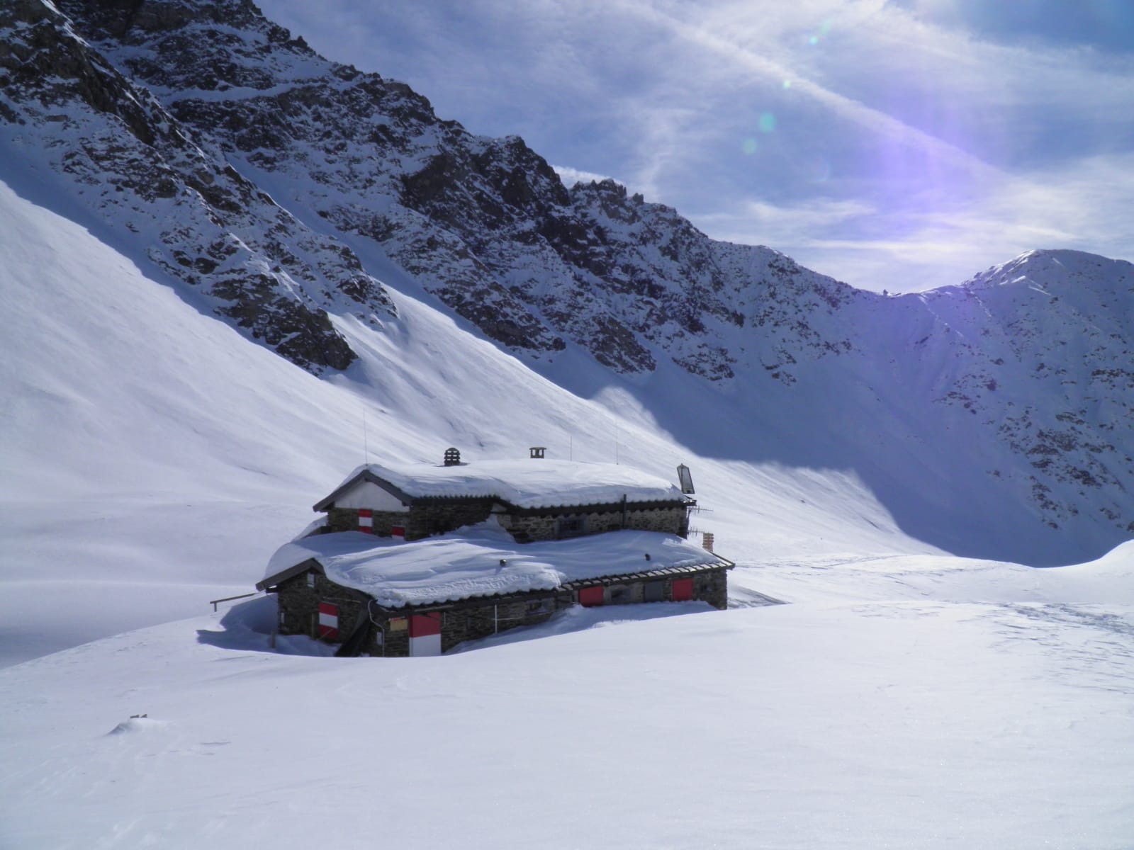 Foto di una abitazione coperta di neve in mezzo a delle montagne coperte completamente di neve