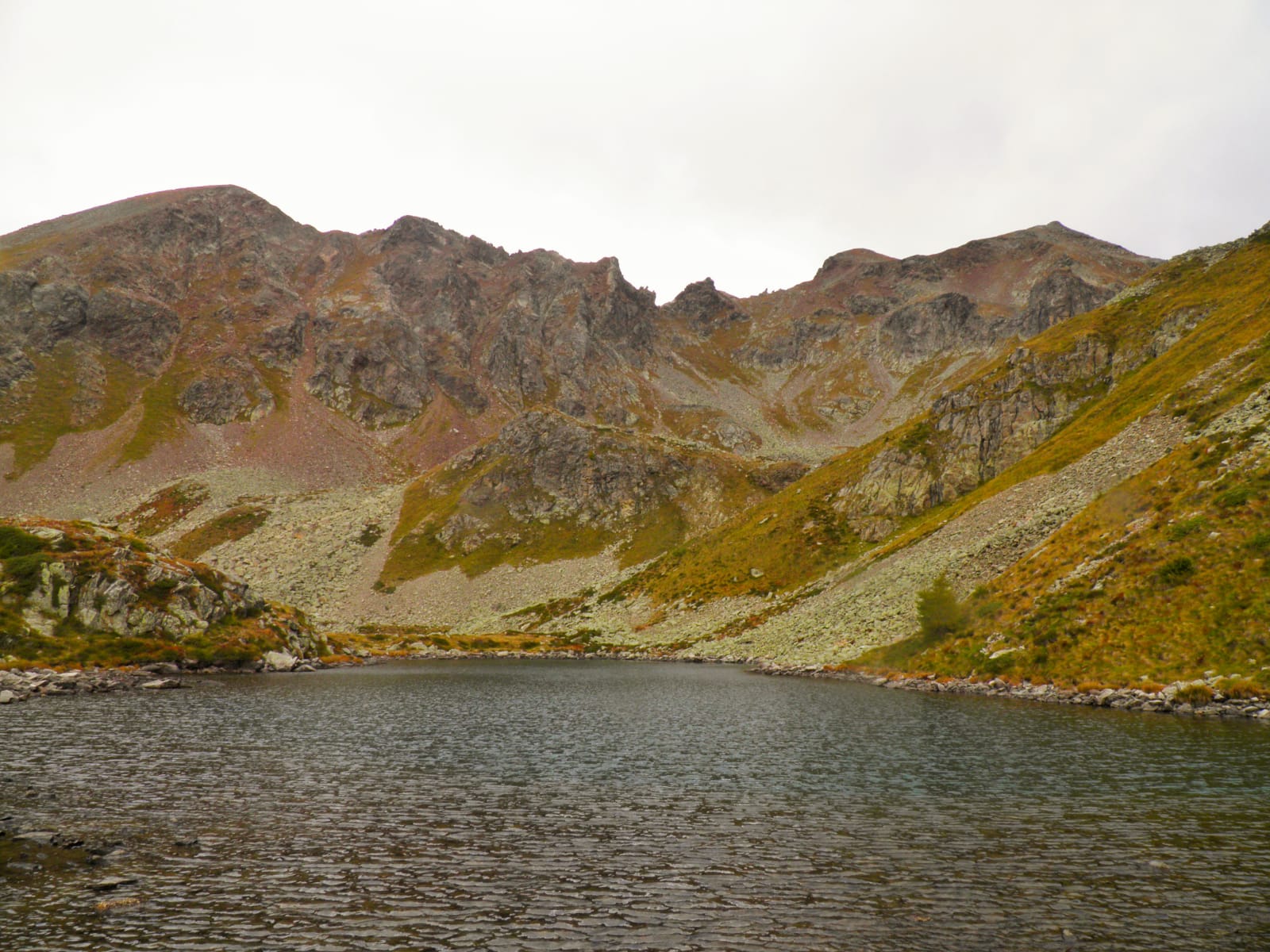 Vista lago circondato da montagne rocciose coperte di un verde quasi appassito