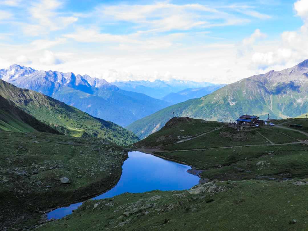 Vista di un piccolo lago vicino ad un rifugio alpino in mezzo alle montagne verdi con un cielo sereno e soleggiato