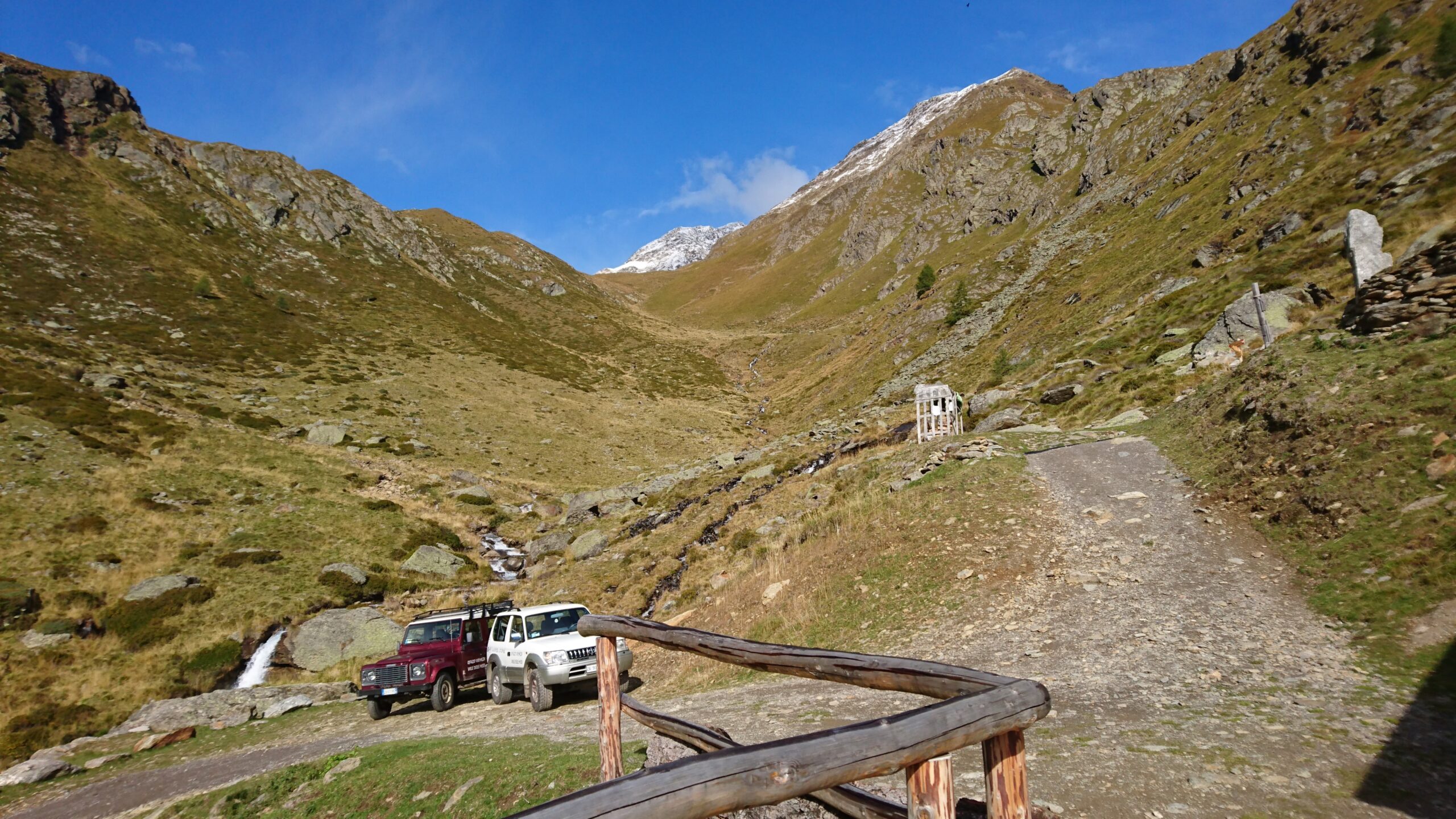 Vista montagne coperte di un verde pallido ed un sentiero sterrato e due automobili una bianca e l'altra rossa