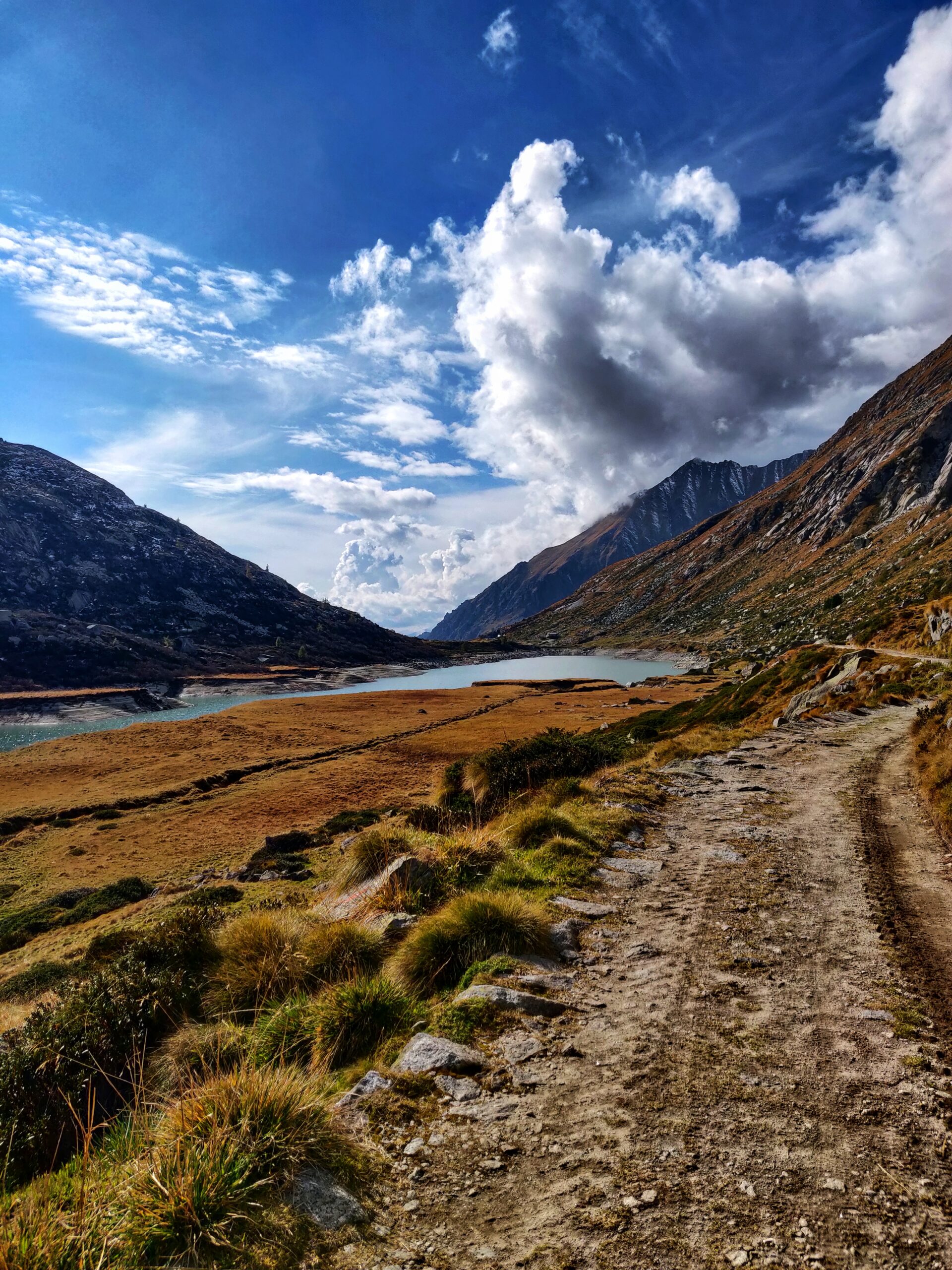 Vista sentiero sterrato che porta ad un lago in mezzo alle montagne