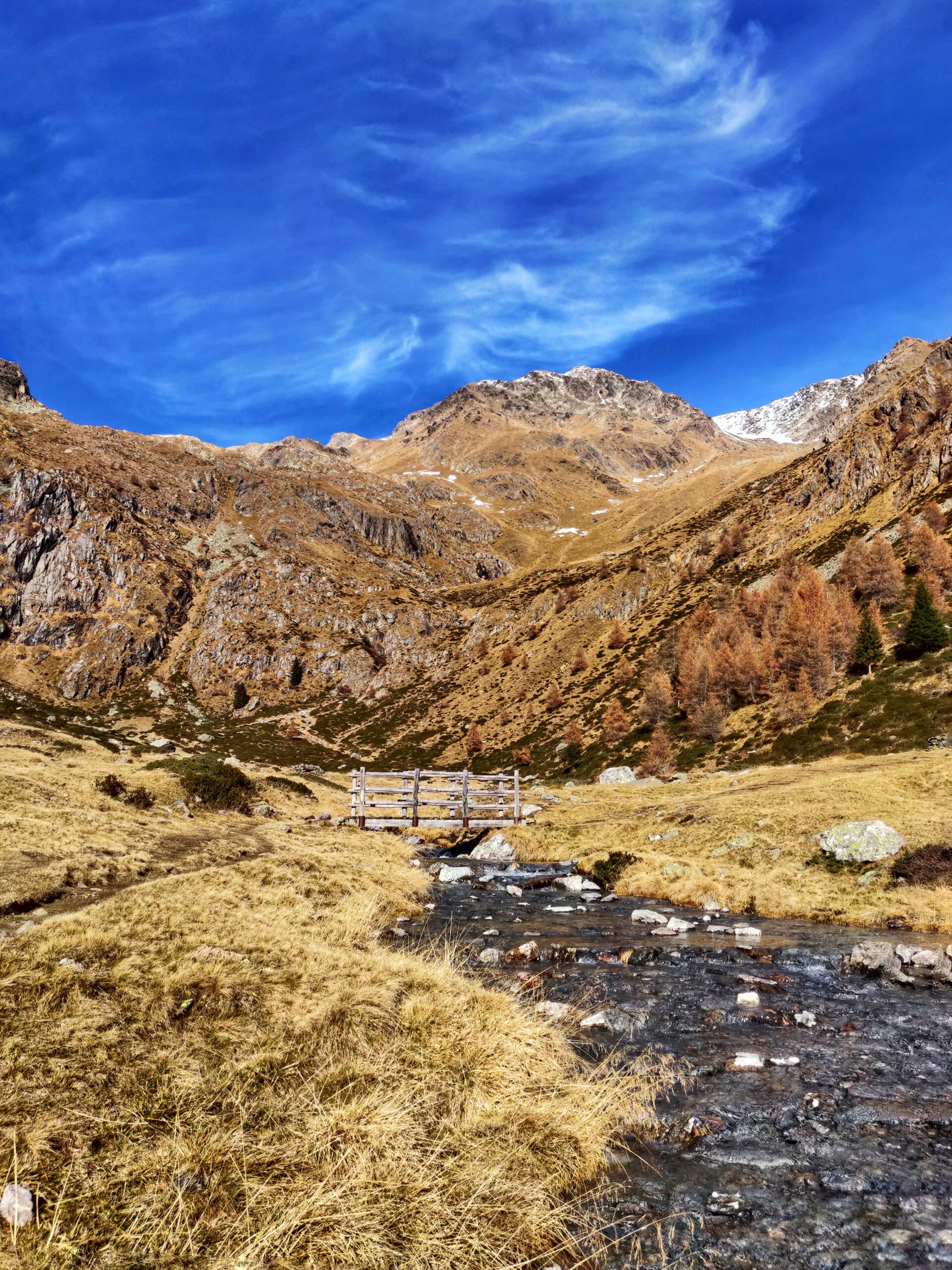 Vista di un piccolo sentiero d'acqua con un piccolo ponte da attraversare per raggiungere le montagne da entrambi i lati