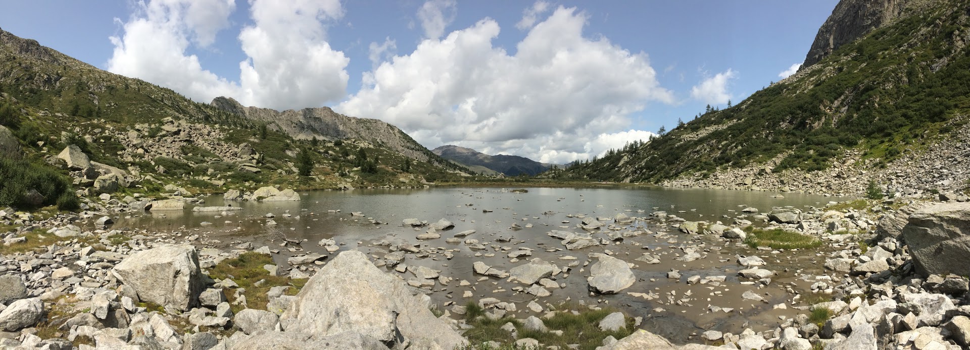 Foto di un lago colmo di piccole e grandi rocce in mezzo alle montagne verdi