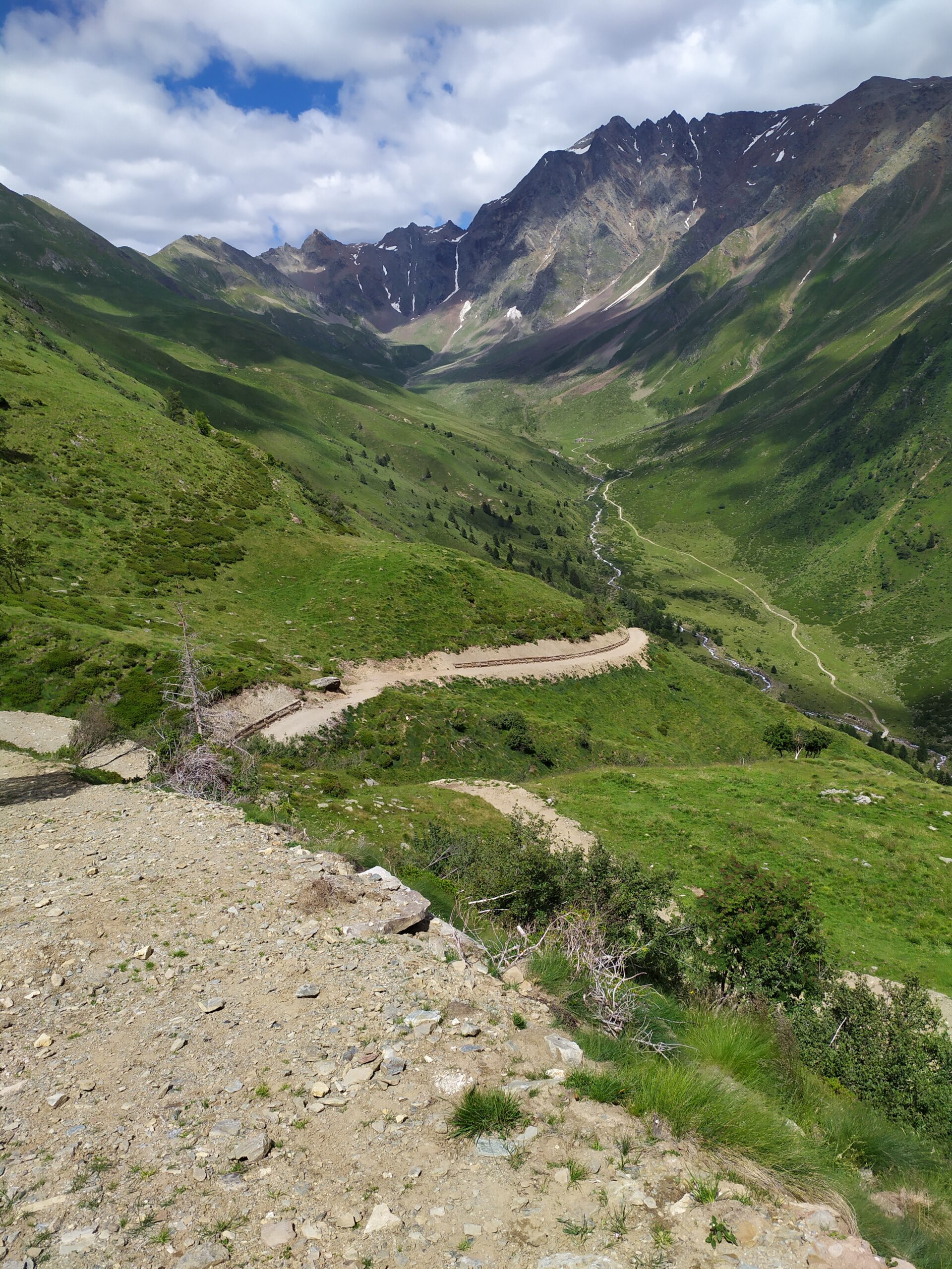 Foto di un piccolo sentiero quasi interminabile in mezzo a delle montagne ricoperte di piante verdi e un cielo brillante e poche nuvole